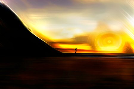 A silhouette of a person standing on a beach at sunset. The sky is orange and the sun is setting.