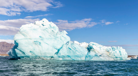 A large blue ice block floating in the ocean. The sky is clear and blueの写真素材