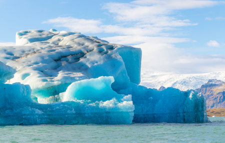 A large blue ice block is floating in the ocean. The sky is clear and the water is calmの写真素材