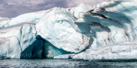 A large ice block with a hole in it. The ice is blue and white. The water is calm