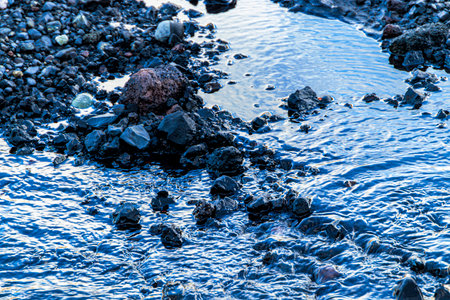 A rocky shoreline with a body of water in the foreground. The water is murky and the rocks are scattered throughout the sceneの写真素材