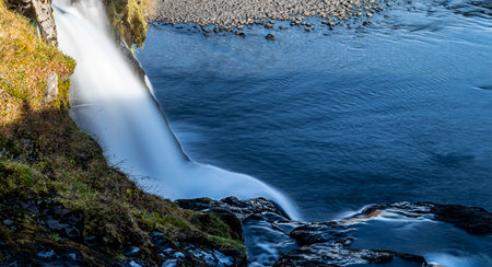 A waterfall is flowing into a body of water. Silk effect.. The water is clear and calm. The scene is peaceful and sereneの写真素材