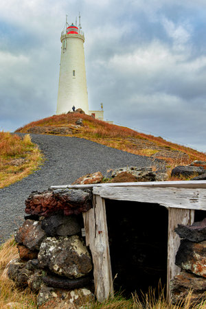 Reykjanesta lighthouse. On top of a hill with a cloudy sky in the background. The lighthouse is surrounded by rocks and a wooden structureの写真素材