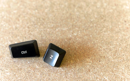 Two black keys are laying on a wooden surface. One of the keys is labeled CTRL and the other is...