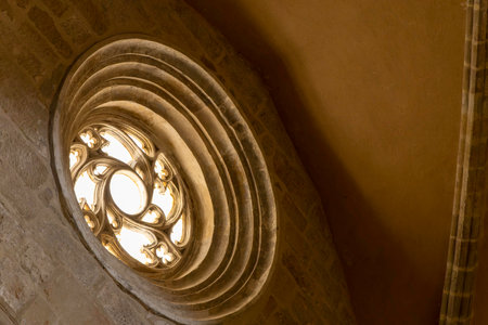 A window with a circular design is lit up by the sun. Gothic rose window. The light shines through the window, creating a warm and inviting atmosphereの写真素材