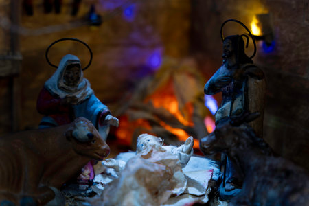 A nativity scene with a man and woman kneeling over baby Jesus. They are slightly illuminated by the light of the moon and a bonfireの写真素材