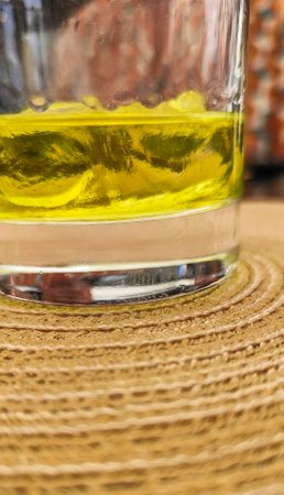 A glass of yellow liquor on the rocks sits on a table. The liquid appears to be a mixture of two different colors, possibly a cocktail or a drink with a unique colorの写真素材