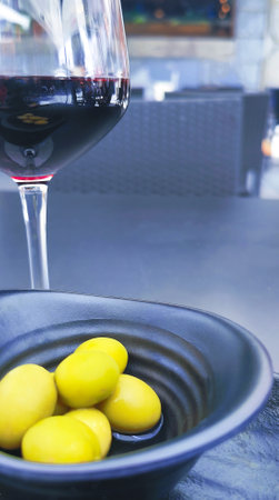 A glass of red wine is poured close to a black bowl with olives. The bowl is placed on a tableの写真素材