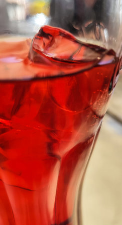 A glass of red liquid with ice cubes in it. The ice cubes are melting and the liquid is a deep red color. The glass is almost full.の写真素材