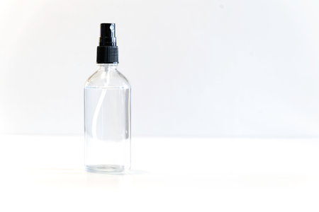 Small glass bottle with spray cap on bright background. The bottle is filled with a transparent liquidの写真素材