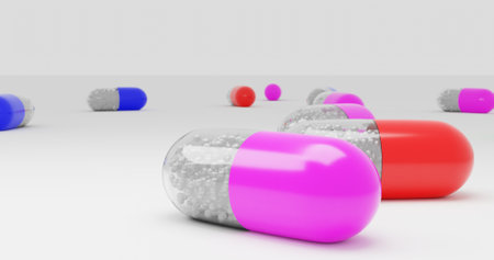 A row of pills are shown in various colors, including red, pink and blue. The pills are scattered across a white surfaceの写真素材