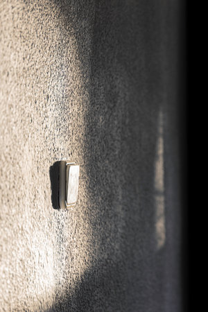 A white wall with a light switch on it. Sunlight illuminates part of the wall