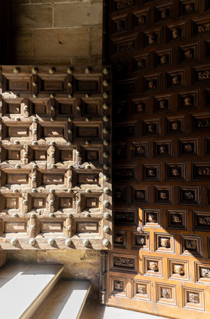 Detail of the entrance to the cathedral of Porquenza. Two ancient wooden doors display intricate medieval-style designs. The sunlight is shining through the door, creating a warm and inviting atmosphereの写真素材