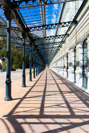 A long, narrow walkway with a lot of metal poles and a lot of sunlight. The shadows cast by the poles create a sense of depth and movement. Exterior facade of Canfranc International Stationの写真素材