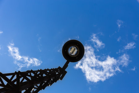 An industrial style street lamp, constructed from steel bars, stands out against an intensely blue sky. The lamp post seems to await the arrival of night, giving a sense of vigilance and protection.の写真素材