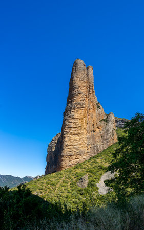 One geological formation of vertical walls in Mallos de Riglos, Huesca, Spain. The mountain is surrounded by trees and the sky is clearの写真素材