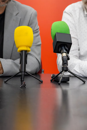Two unrecognizable men hold a press conference. On the table in front of them are two microphones....