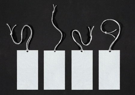 Four white labels with strings hanging from them.The labels are made of thick cardboard with an elegant texture, and they are over a dark backgroundの写真素材