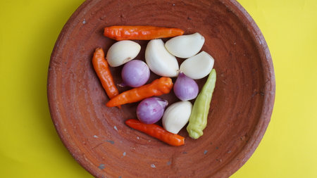 garlic, onion, and chili in a stone bowl. Isolated on yellow background.の写真素材
