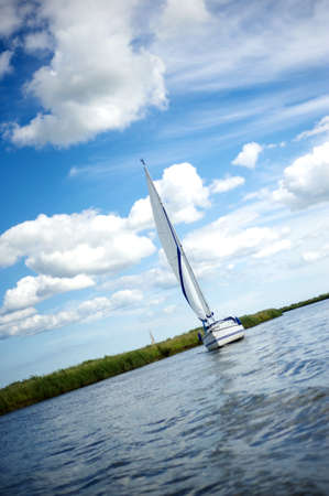 Norfolk Broads blue and white sail boat sailing down the river on a summer day