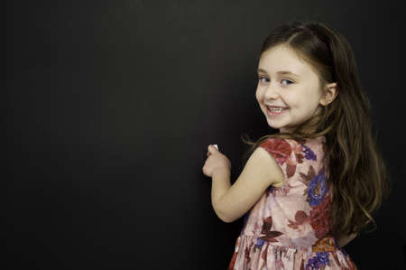 Smart young girl wearing a red dress writing on a blackboardの写真素材