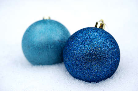 Two Glittered Blue Christmas baubles placed together in the snowの写真素材