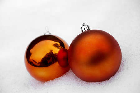 One frosted and one reflective orange Christmas bauble, placed together in the snowの写真素材