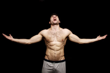 Topless man looking up shouting with his arms outstretched on a black background