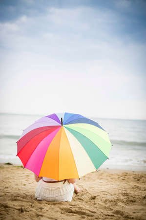 Girl sat on the beach with a large colourful umbrellaの写真素材