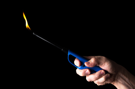 Burning gas lighter in a man's hand isolated on black background