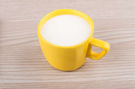 Yellow cup of milk on wooden tableの写真素材