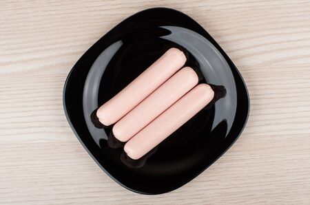 Three small raw sausage in black glass plate on table, top viewの写真素材
