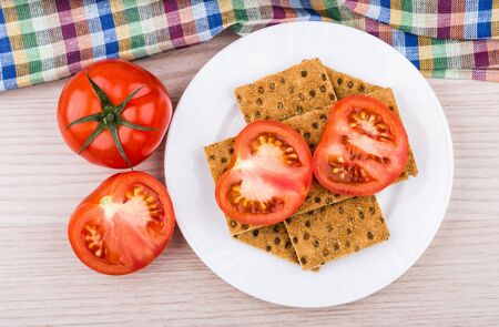 Wheat crisp bread in plate tomatoes and towel on wooden table top viewの写真素材