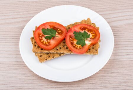 Wheat crisp bread with slice of tomatoes in white glass plate on tableの写真素材