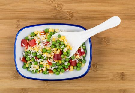 Vegetable mix in blue bowl on wooden bamboo board and plastic spoon, top viewの写真素材