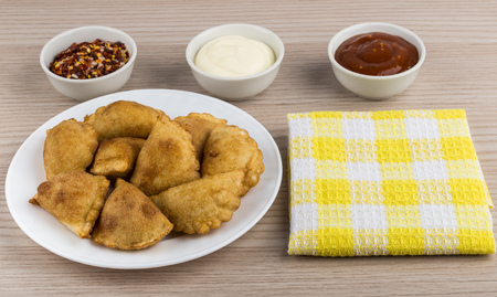 White plate with small pasties, bowls with sauce, spices and napkin on tableの写真素材