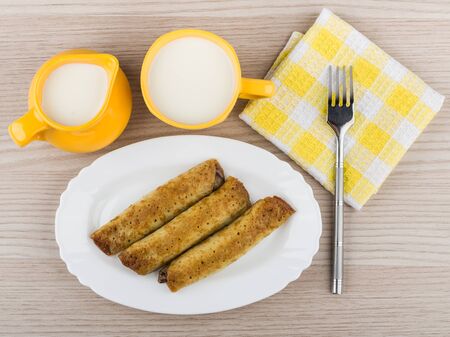 Pancake stuffed in white dish, cup milk, napkin and fork on wooden table, top viewの写真素材