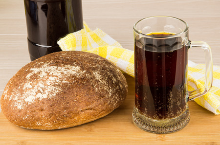 Russian kvass in bottle and mug, round loaf of bread on wooden board