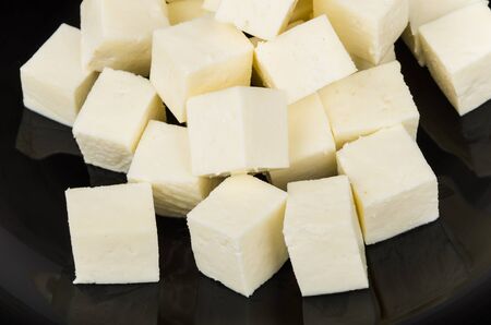 Close up of cheese in form of cubes on glass black plateの写真素材