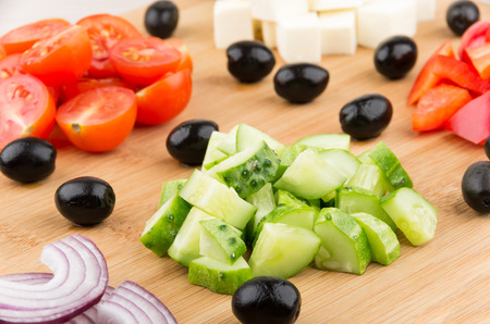 Slices of onions tomatoes peppers cucumbers cheese and black olives on wooden boardの写真素材