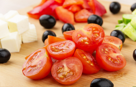 Slices of cheese tomatoes peppers cucumbers and black olives on wooden boardの写真素材