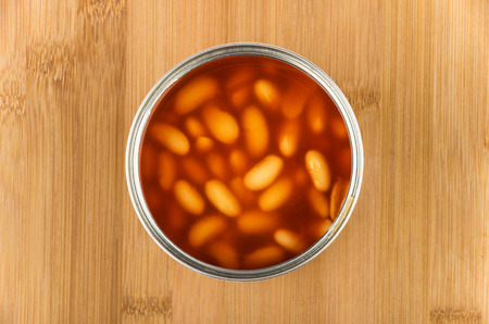 Open metal cans with beans in tomato sauce on wooden board top viewの写真素材
