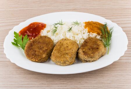 Fried cutlet with rice squash caviar ketchup and greens in dish on tableの写真素材