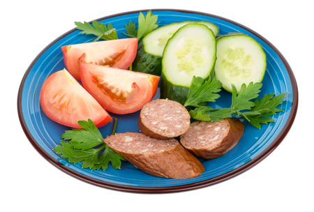 Plate with pieces of sausage, tomatoes, cucumbers and parsley isolated on white backgroundの写真素材