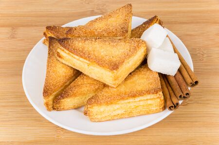 Sweet puff pastries, pieces of  lumpy sugar and cinnamon sticks in glass plateの写真素材