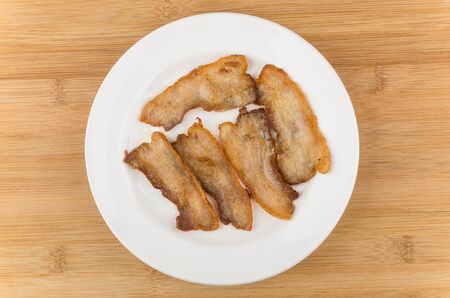 Pieces of fried bacon in glass plate on wooden table, top viewの写真素材