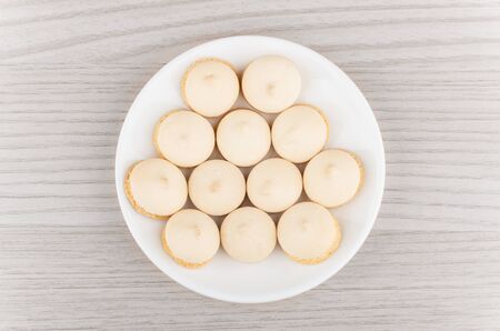 Cookies with egg glaze in white saucer on wooden table, top view