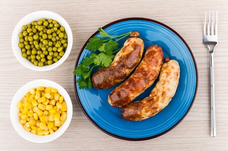 Grilled sausage in plate with parsley, green peas and sweet corn on wooden table, top viewの写真素材