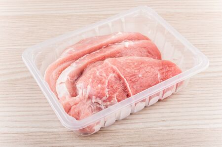 Pieces of raw pork in plastic box on wooden tableの写真素材