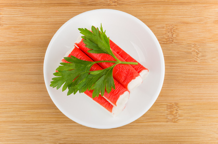 Crab sticks with parsley in white saucer on wooden tableの写真素材